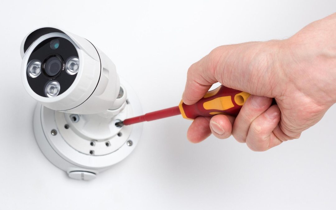 Technician installing white bullet CCTV camera on wall using screwdriver